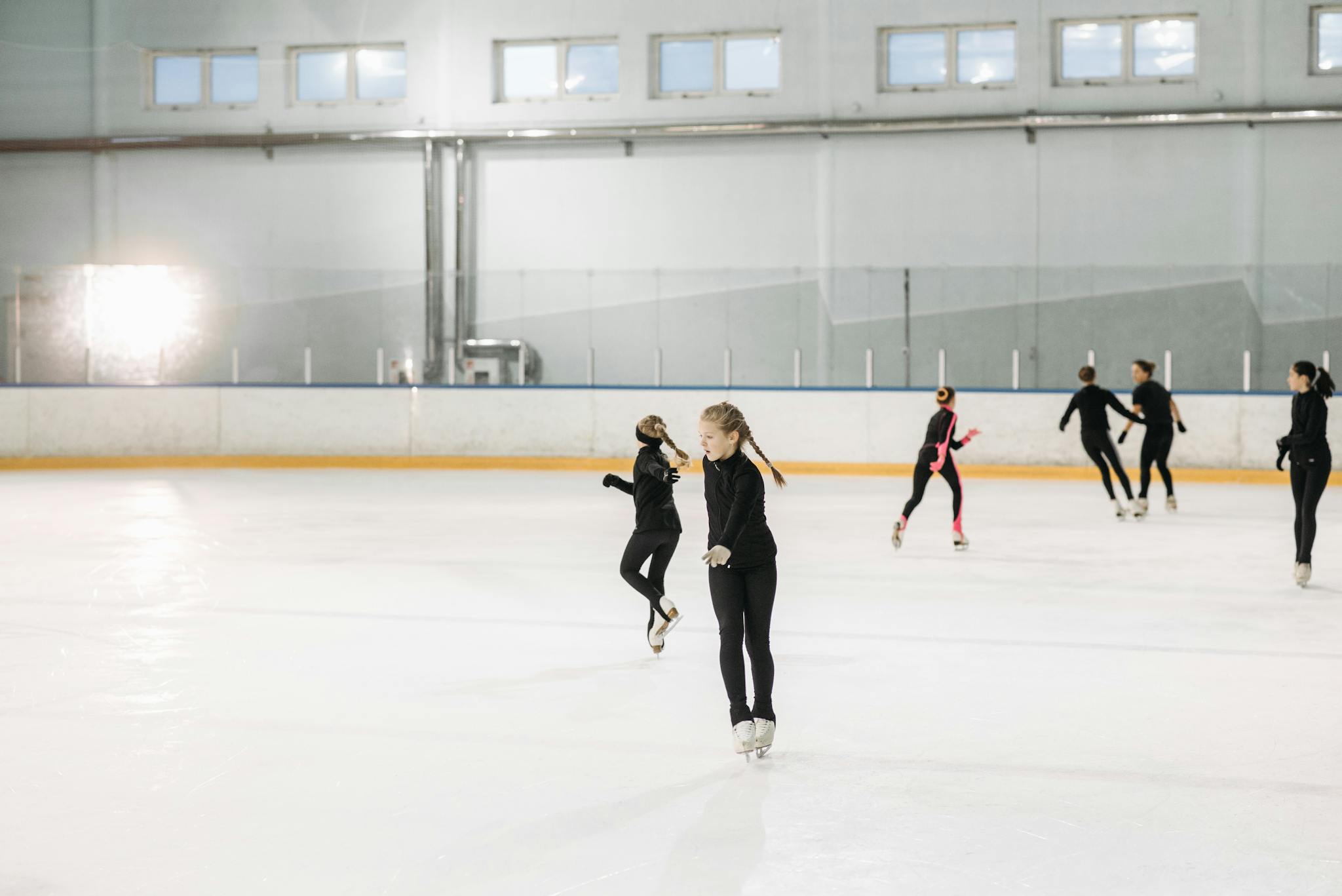 A group of young figure skaters practicing indoors on an ice rink, honing their skills.