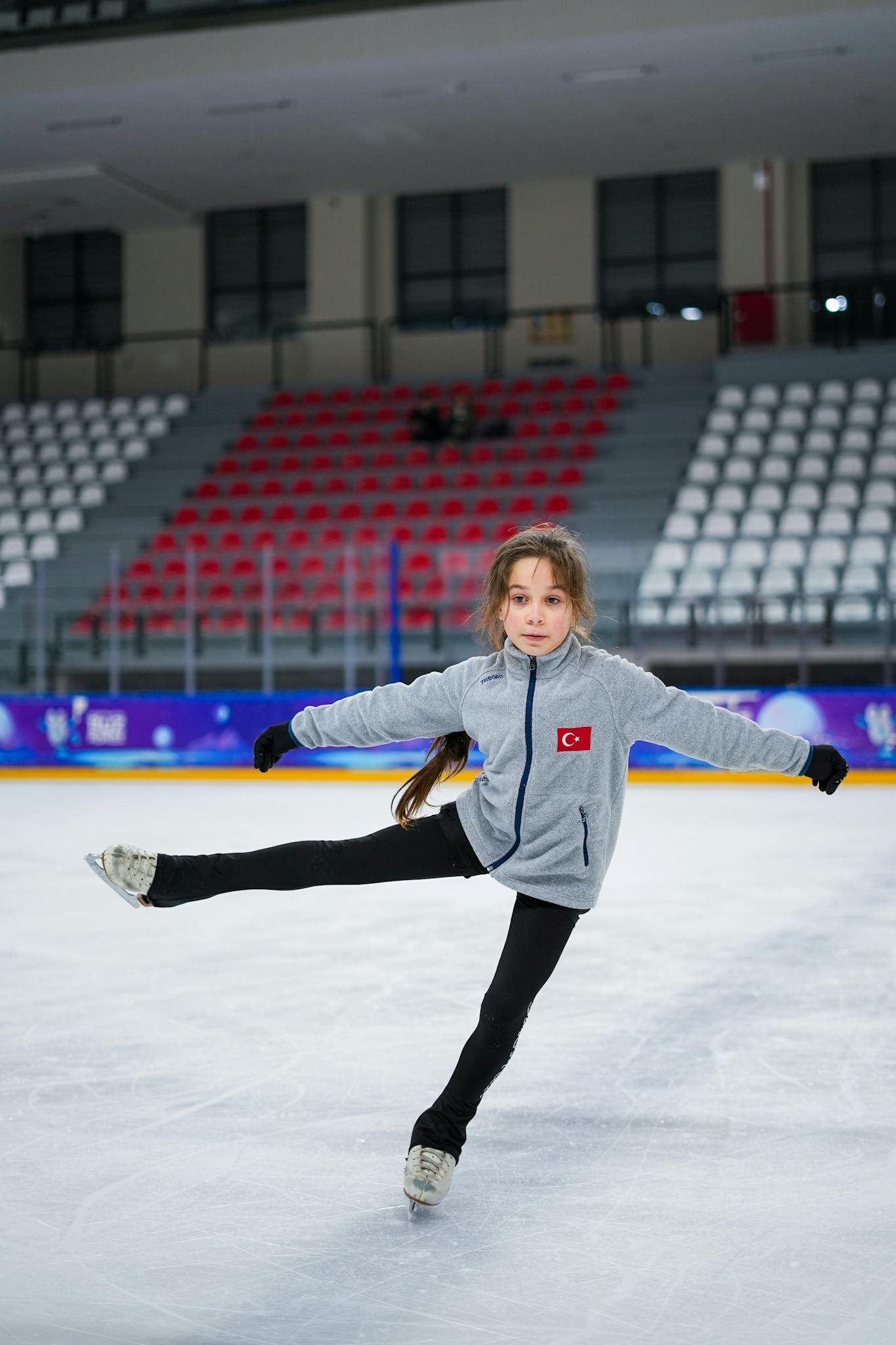 A young girl practices figure skating on an indoor ice rink, showcasing balance and skill.